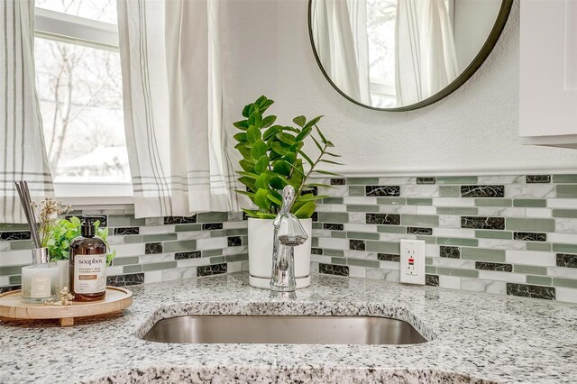 kitchen view of tasteful backsplash, a sink, and light stone counters