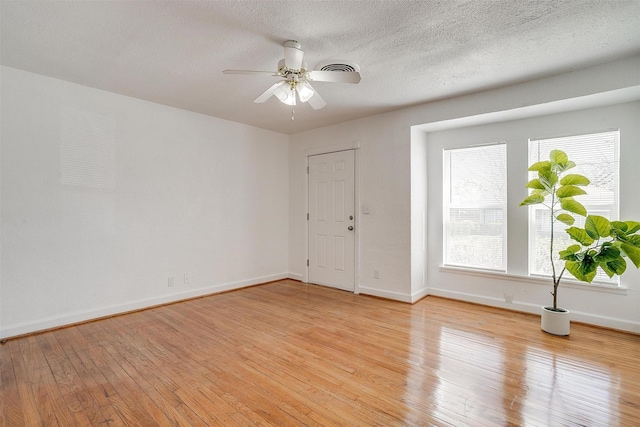 unfurnished room featuring ceiling fan, light wood-style flooring, baseboards, and a textured ceiling