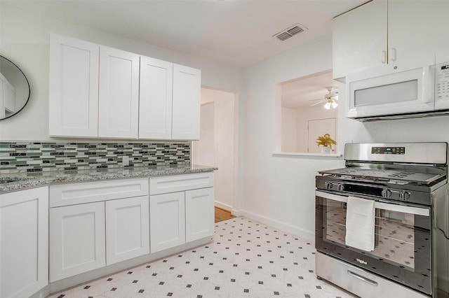 kitchen with white microwave, stainless steel gas range oven, light flooring, baseboards, and white cabinetry