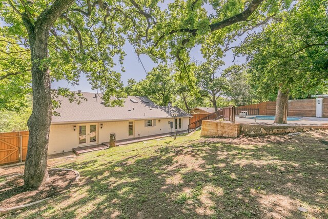 rear view of property with french doors, a fenced backyard, and a shingled roof