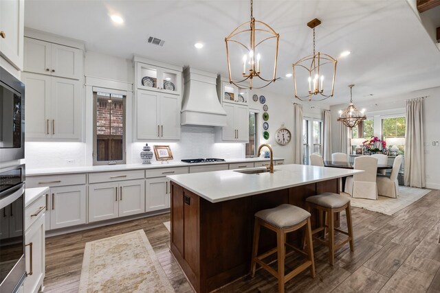 kitchen with a sink, premium range hood, a chandelier, appliances with stainless steel finishes, and dark wood-style floors