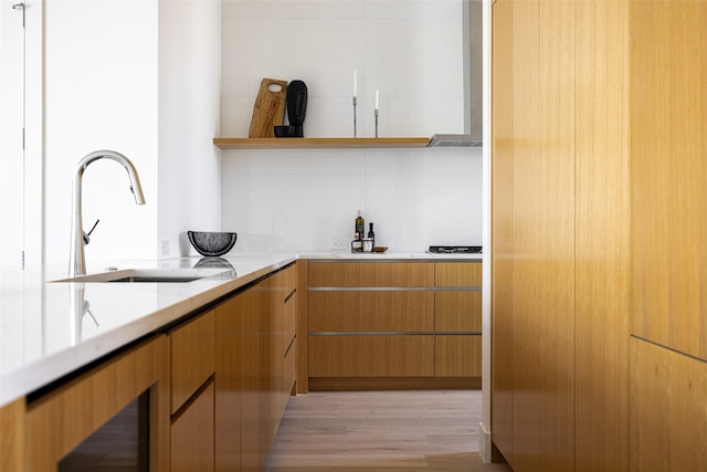 kitchen featuring a sink, light wood finished floors, open shelves, wall chimney range hood, and light stone countertops