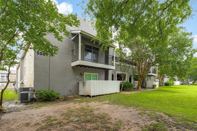 rear view of property featuring central AC, stucco siding, a balcony, and fence