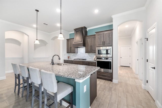 kitchen with appliances with stainless steel finishes, a sink, custom exhaust hood, a kitchen breakfast bar, and light stone countertops