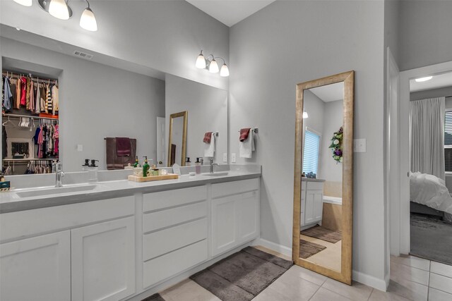 ensuite bathroom with tile patterned flooring, double vanity, and baseboards