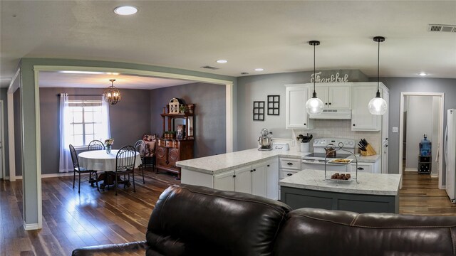 kitchen featuring white appliances, under cabinet range hood, dark wood finished floors, white cabinets, and a peninsula