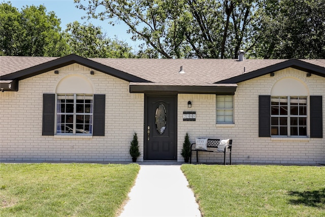 single story home with roof with shingles, a front lawn, and brick siding