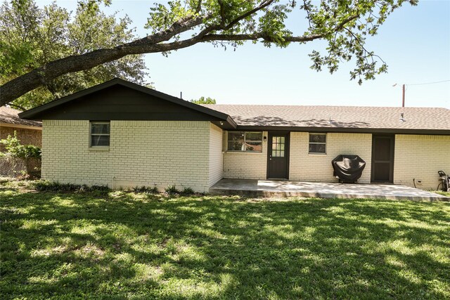 rear view of house featuring brick siding, a patio, a lawn, and roof with shingles