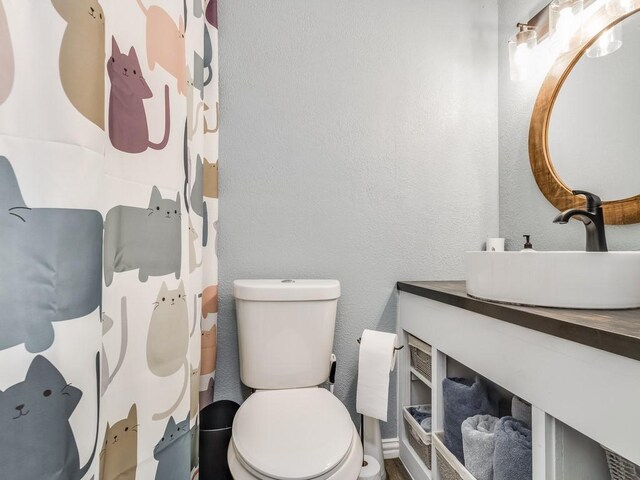 full bath with toilet, a textured wall, and vanity