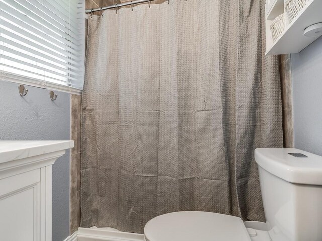bathroom featuring toilet, curtained shower, and a textured wall