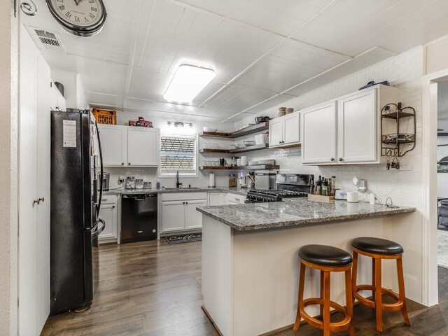 kitchen featuring black appliances, a sink, a peninsula, dark wood finished floors, and light stone counters