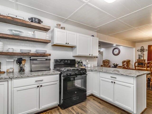 kitchen featuring black gas range oven, a peninsula, wood finished floors, white cabinetry, and backsplash