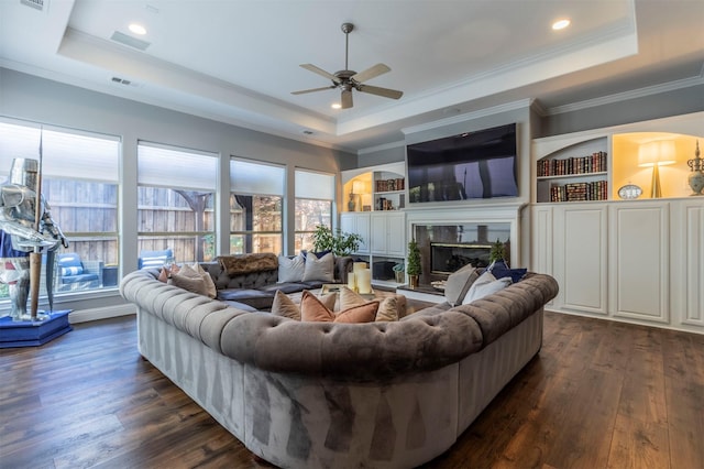 living room with a tray ceiling, crown molding, ceiling fan, dark wood finished floors, and a premium fireplace