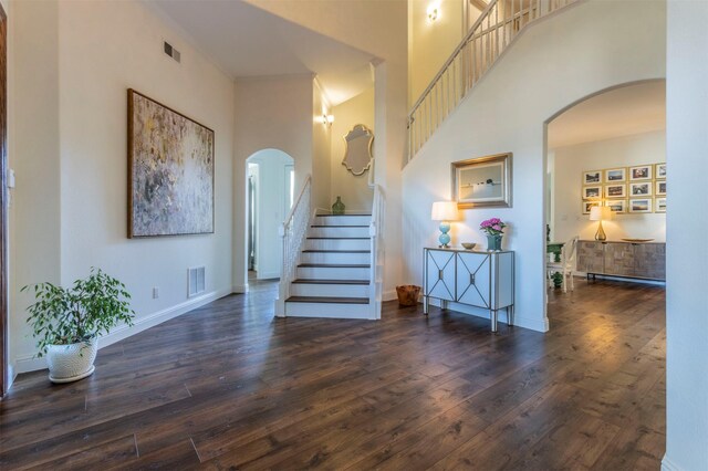 stairway featuring a towering ceiling, hardwood / wood-style flooring, arched walkways, and baseboards