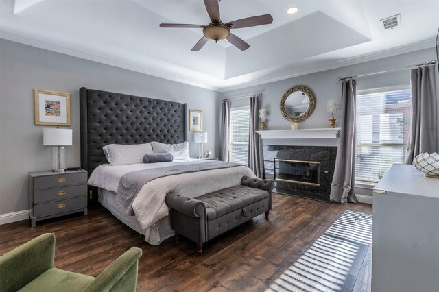 bedroom featuring a raised ceiling, multiple windows, ornamental molding, a premium fireplace, and wood finished floors