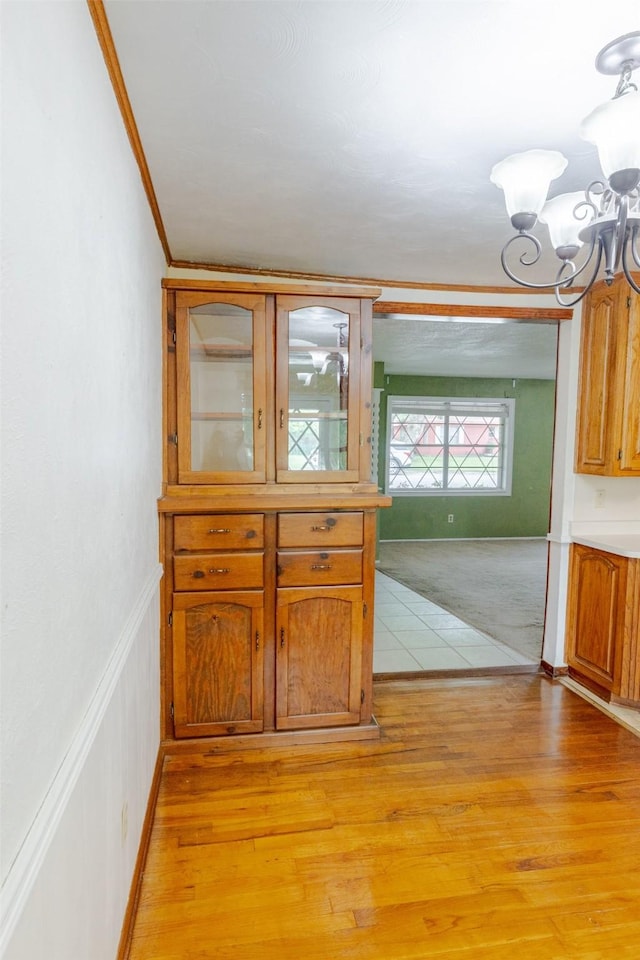 1809 Stevens St, Bridgeport, TX 76426 - kitchen featuring crown molding, a chandelier, light wood finished floors, brown cabinetry, and glass insert cabinets