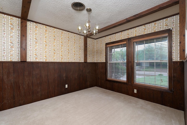 carpeted empty room with wallpapered walls, a chandelier, a textured ceiling, a wainscoted wall, and wooden walls