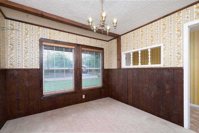 unfurnished room with a chandelier, ornamental molding, wallpapered walls, and a wainscoted wall
