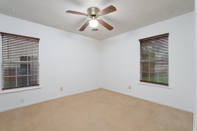 empty room featuring light carpet, ceiling fan, a textured ceiling, and baseboards