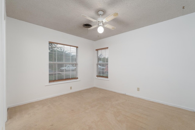 spare room with a textured ceiling, light carpet, a ceiling fan, and baseboards
