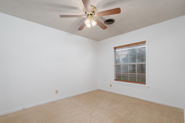 empty room featuring a textured ceiling, light carpet, a ceiling fan, and baseboards