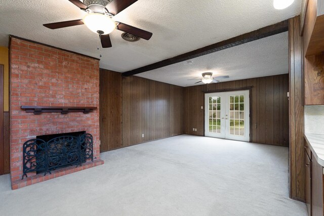 unfurnished living room with a ceiling fan, french doors, wood walls, beam ceiling, and light colored carpet