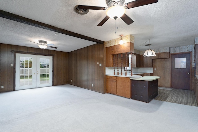 kitchen featuring a peninsula, light carpet, light countertops, wooden walls, and ceiling fan