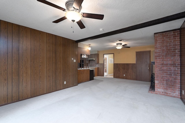 unfurnished living room featuring wooden walls, ceiling fan, light carpet, beam ceiling, and a textured ceiling