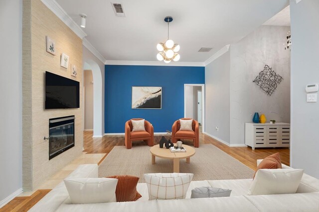 living area with wood finished floors, a tiled fireplace, arched walkways, a chandelier, and crown molding
