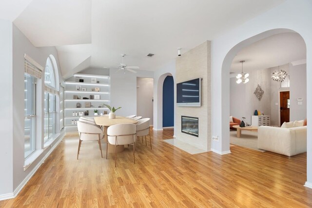 dining space with light wood finished floors, healthy amount of natural light, ceiling fan, a large fireplace, and a high ceiling