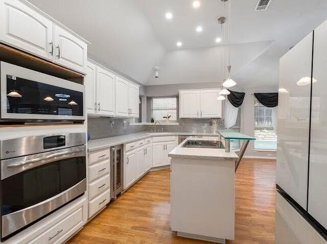 kitchen featuring appliances with stainless steel finishes, wine cooler, white cabinets, a sink, and vaulted ceiling