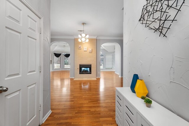 hallway featuring arched walkways, light wood-type flooring, ornamental molding, and baseboards