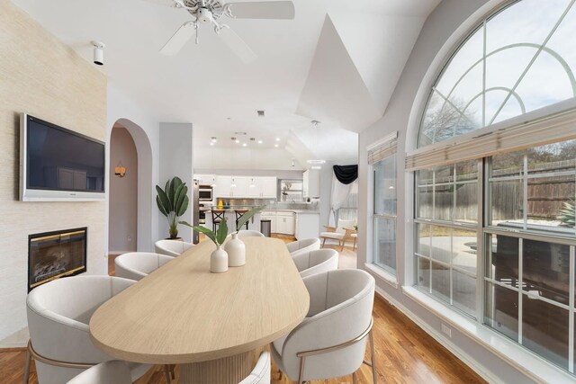 dining area with ceiling fan, a glass covered fireplace, wood finished floors, and arched walkways