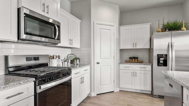 160 Trinity St, Grandview, TX 76050 - kitchen featuring appliances with stainless steel finishes, white cabinetry, decorative backsplash, light stone countertops, and light wood-style flooring