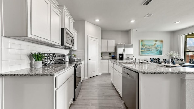 164 Trinity St, Grandview, TX 76050 - kitchen with stainless steel appliances, a kitchen island with sink, white cabinets, light wood-style flooring, and recessed lighting