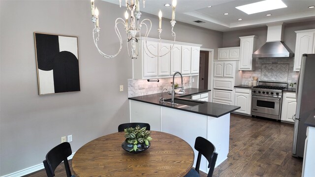 kitchen with wall chimney range hood, stainless steel appliances, dark countertops, white cabinets, and recessed lighting