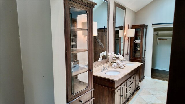 full bath featuring double vanity, vaulted ceiling, and baseboards