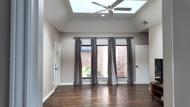 empty room featuring a skylight, a ceiling fan, wood finished floors, baseboards, and vaulted ceiling