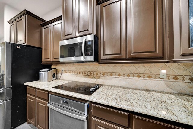 kitchen featuring appliances with stainless steel finishes, backsplash, dark brown cabinetry, and light stone counters