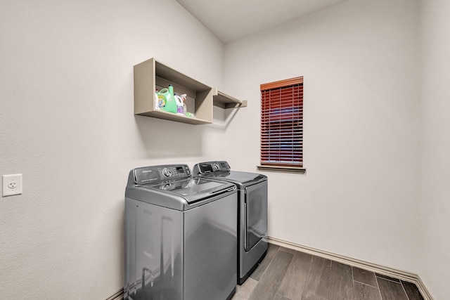 clothes washing area with washing machine and clothes dryer, wood finished floors, and baseboards