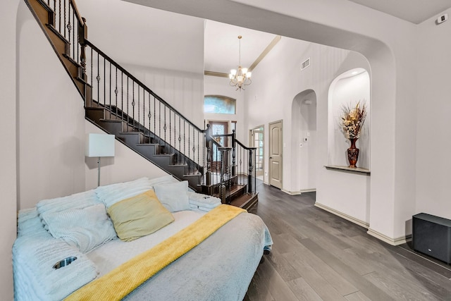 bedroom featuring a chandelier, wood finished floors, baseboards, a high ceiling, and arched walkways