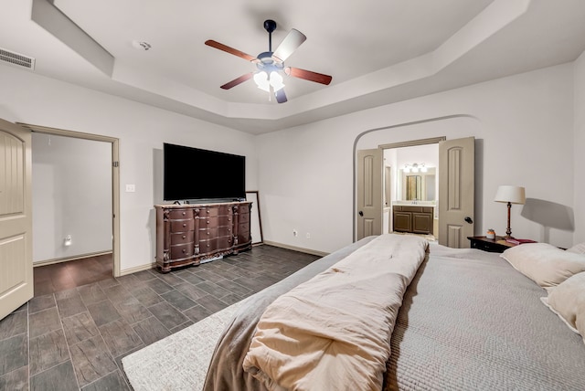 bedroom featuring a tray ceiling, baseboards, wood tiled floors, a ceiling fan, and connected bathroom
