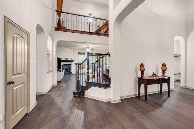 foyer with a ceiling fan, arched walkways, stairway, dark wood-type flooring, and baseboards