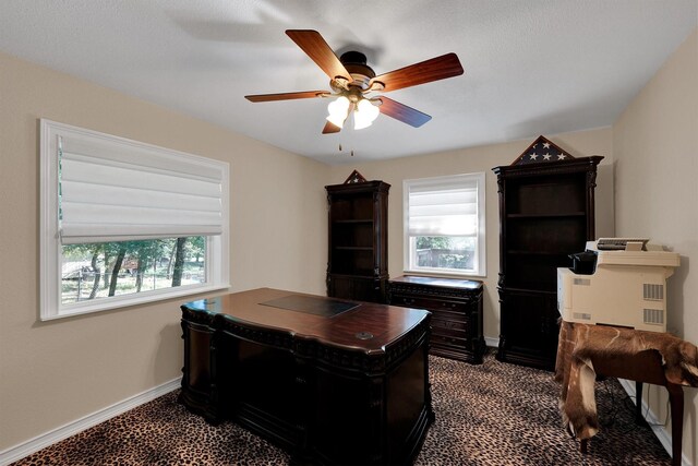 office space with healthy amount of natural light, ceiling fan, baseboards, and dark colored carpet