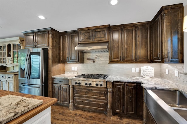kitchen featuring stainless steel appliances, under cabinet range hood, dark brown cabinetry, backsplash, and light stone countertops
