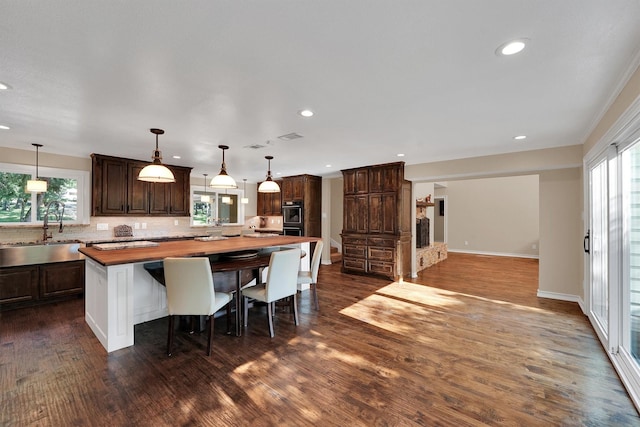 kitchen featuring a sink, wooden counters, dark brown cabinetry, backsplash, and healthy amount of natural light