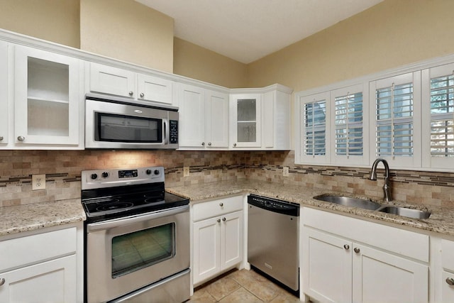 kitchen featuring appliances with stainless steel finishes, a sink, decorative backsplash, white cabinets, and light stone counters