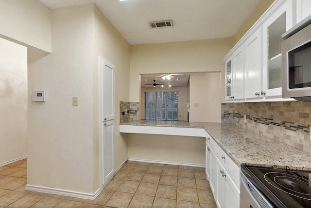 kitchen featuring tasteful backsplash, white cabinetry, light tile patterned floors, and stainless steel microwave