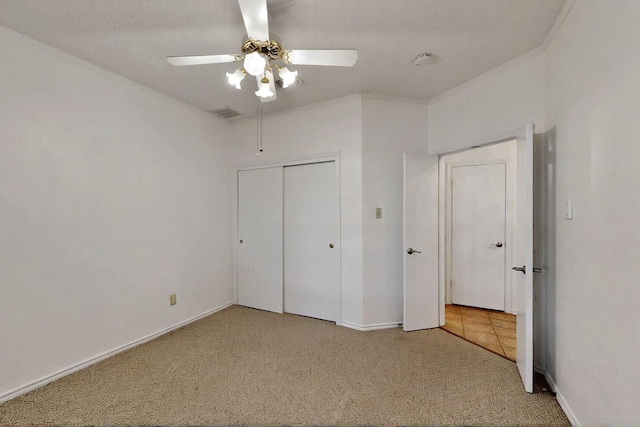 unfurnished bedroom featuring carpet floors, a closet, crown molding, baseboards, and a ceiling fan