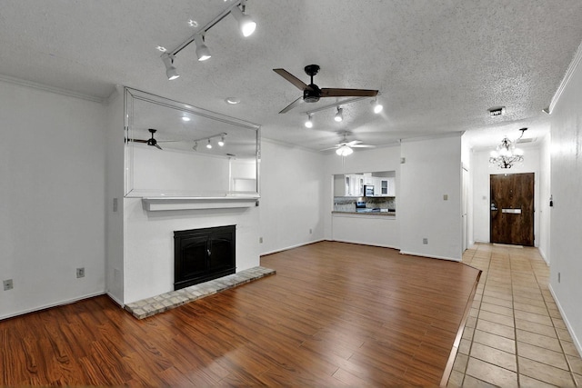 unfurnished living room with ceiling fan, rail lighting, a glass covered fireplace, wood finished floors, and a textured ceiling
